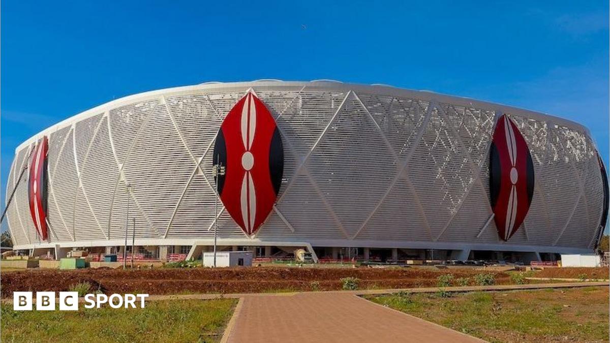 Exterior of a football stadium showing three Kenyan shields in red, white and black on top of a white wrap around