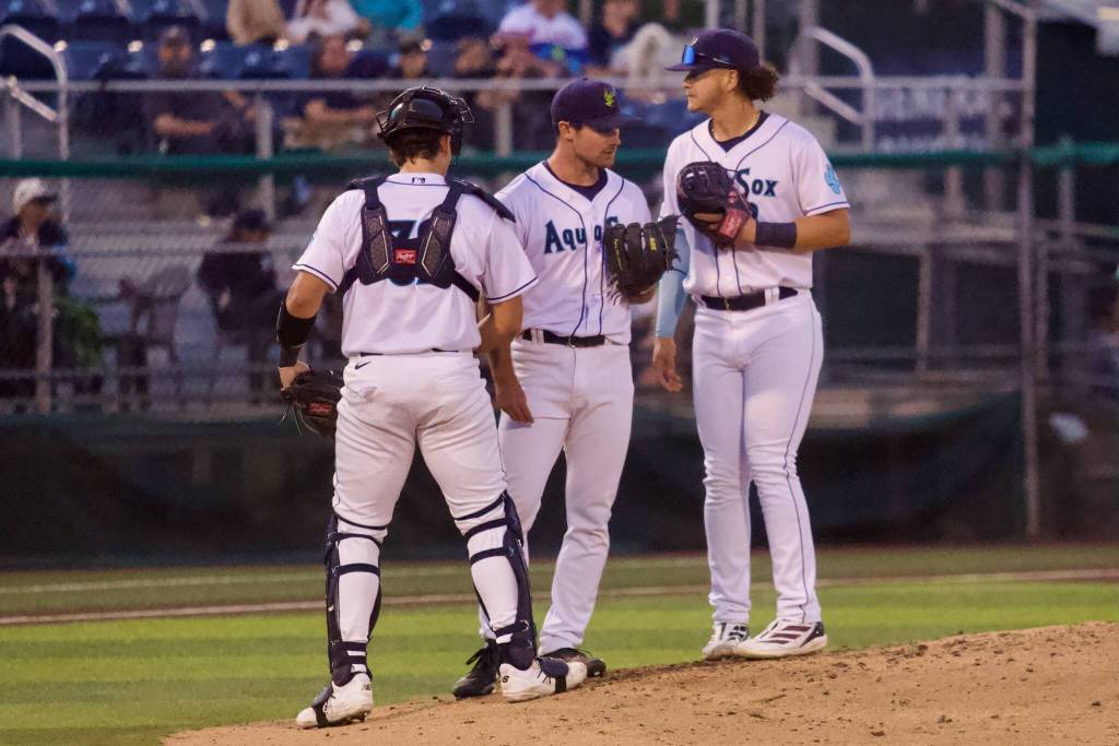 AquaSox pitcher Adam Maier (center) heads back to the rubber after a mound visit with catcher Luke Stevenson (left) and infielder Luis Suisbel during Everett’s 10-4 loss to Eugene at Everett Memorial Stadium on Aug. 25, 2026. (Joe Pohoryles / The Herald)