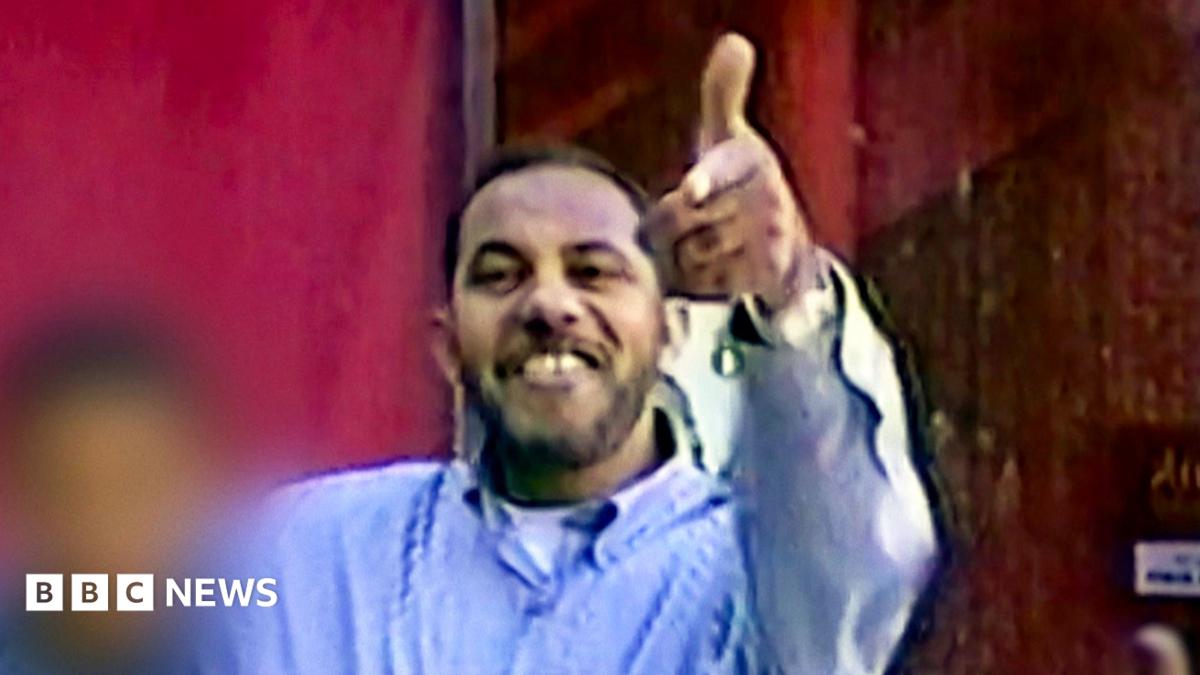 Omar al-Bayoumi in a blue shirt appears to make a gun sign with his hand