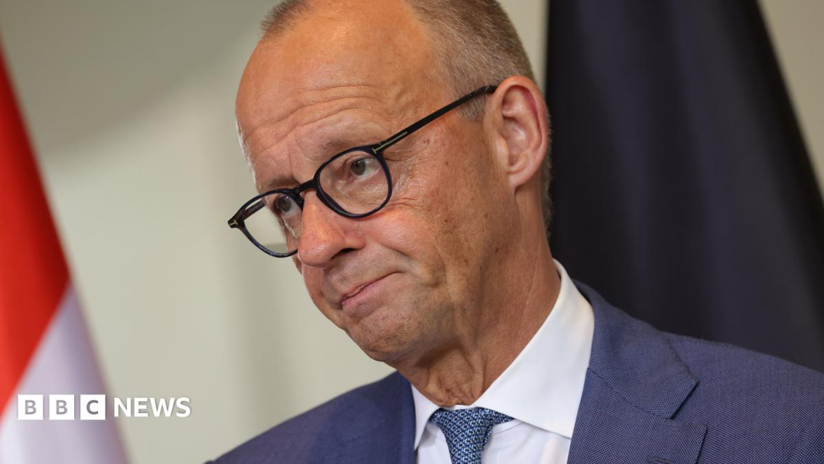 German Chancellor Friedrich Merz appears at a news conference wearing a blue suit and tie, white shirt and glasses.