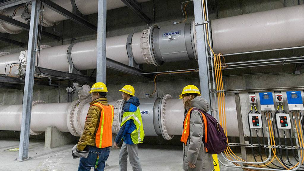 People walk through a subterranean corridor filled with giant pumps and pipes at the Brightwater Wastewater Treatment Plant on Saturday, Feb. 21, 2026 in Woodinville, Washington. (Olivia Vanni / The Herald)