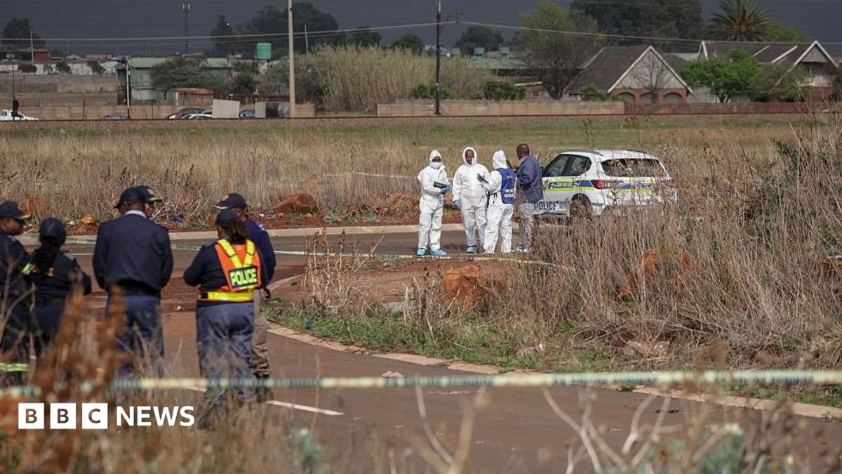 Members of the South African Police Service Forensic Pathology Services dressed in white protective gears work on a crime scene with police with their car nearby