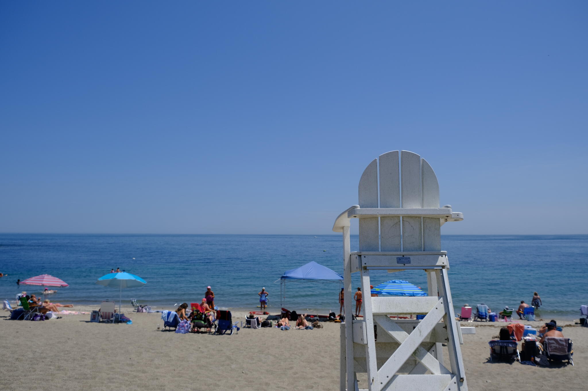 Beachgoers sit throughout Peggotty Beach in Scituate on July 2, 2026. (Patrick Madden/WBUR)