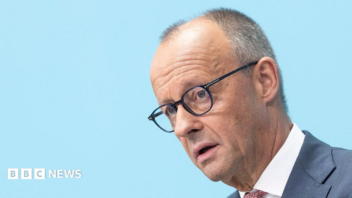Friedrich Merz, wearing black-rimmed glasses and a blue suit, looks just off camera.
