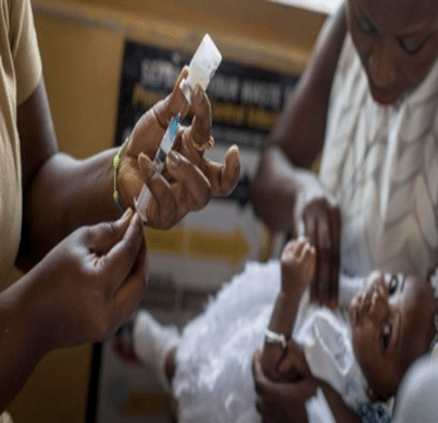 Healthcare workers administer a vaccine to a baby during a clinic visit, with one person holding the baby and another preparing a syringe.