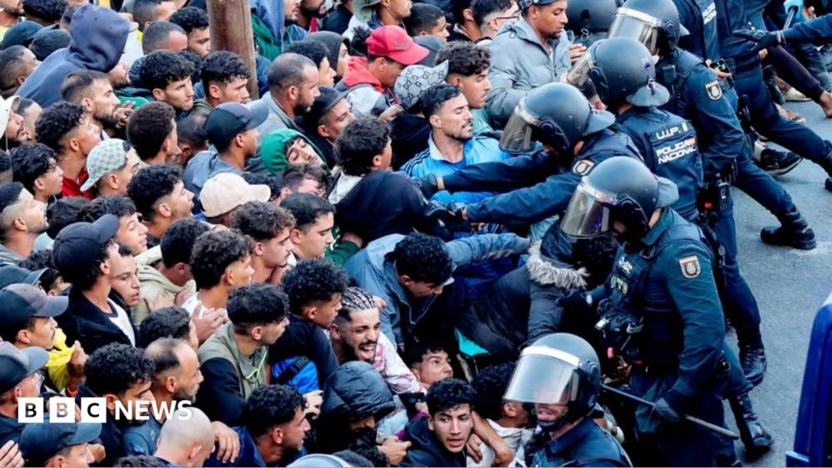 Police officers in riot gear push back a densely packed crowd of migrants during a chaotic transfer operation in Ceuta's port area
