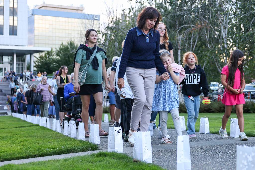 Debbie Warfield holds the hand of her granddaughter Spencer McHargue as they walk through the Snohomish County Campus for a candlelight vigil during “A Night to Remember, A Time to Act” event for Overdose Awareness Day on Thursday, Aug. 27, 2026 in Everett, Washington. (Olivia Vanni / The Herald)