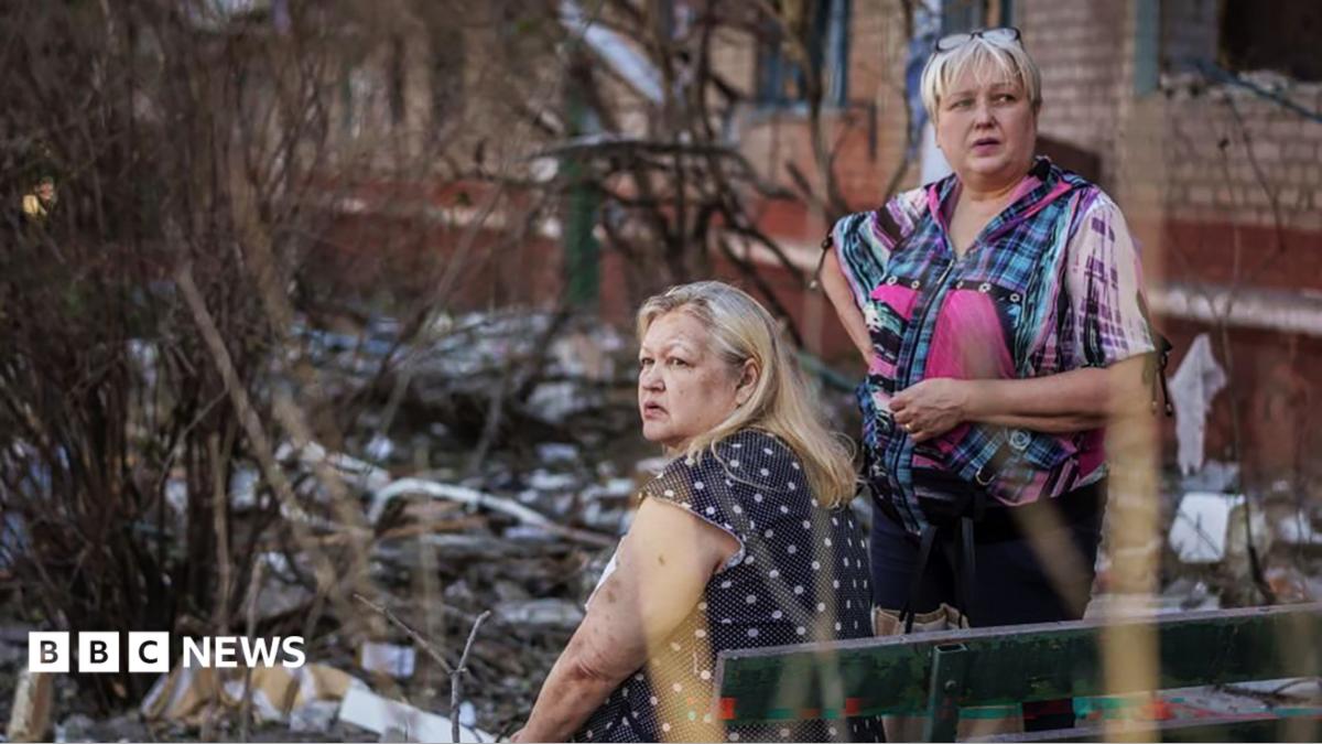 Two middle-aged women stare into the distance amid the rubble from a Russian attack
