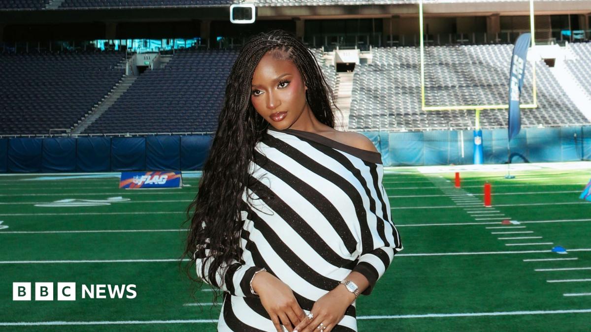Ayra Starr poses on NFL football pitch. She wears a black and white striped dress.