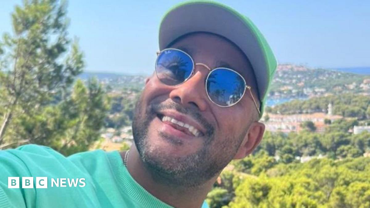 A man wearing, sunglasses, a green top and a green hat. He's smiling at the camera.