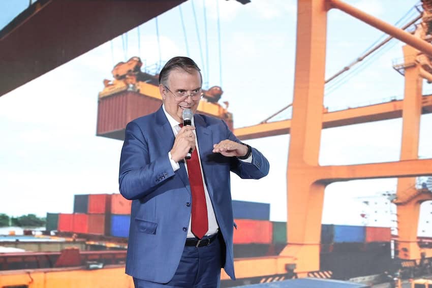 Ebrard standing in front of a presentation featuring an image of shipping containers