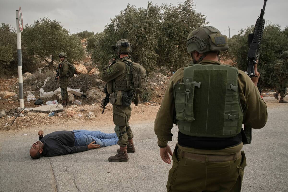 Israeli soldiers stand beside a wounded Palestinian man lying on a road after soldiers shot him ...