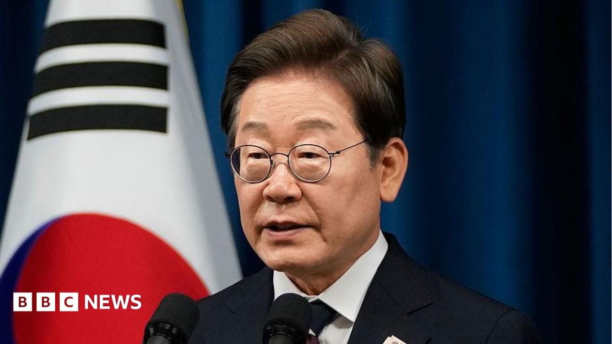 South Korean President Lee wearing a suit and speaking in front of a microphone