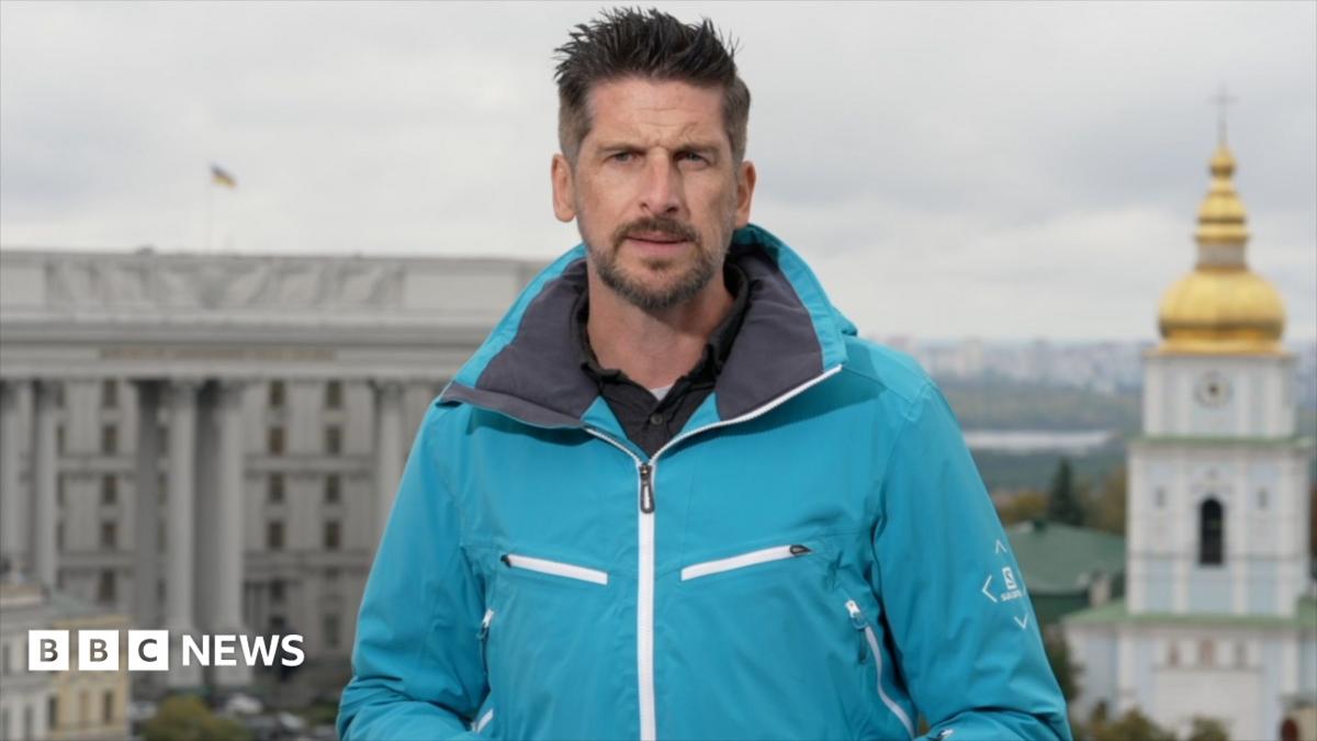 Man in a blue windbreaker standing in front of Kyiv landmarks